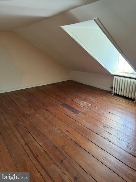 additional living space with lofted ceiling with skylight, radiator, and hardwood / wood-style floors