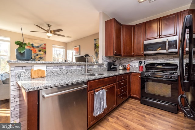 kitchen with black appliances, sink, light hardwood / wood-style flooring, light stone countertops, and kitchen peninsula