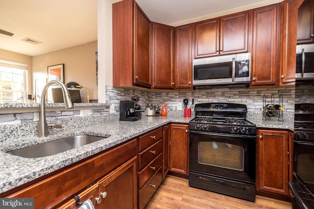 kitchen with black range with gas stovetop, light wood-type flooring, sink, and tasteful backsplash