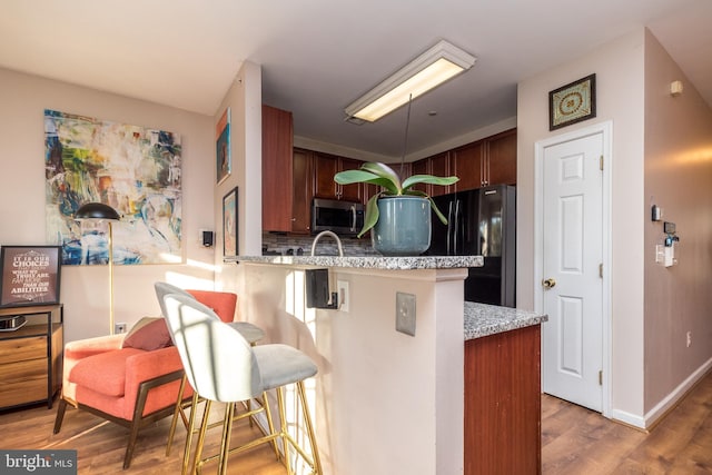 kitchen with black fridge, hardwood / wood-style flooring, tasteful backsplash, kitchen peninsula, and a breakfast bar area