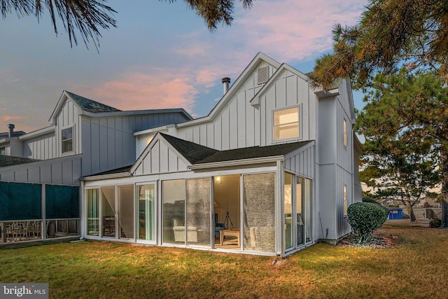 back house at dusk featuring a lawn