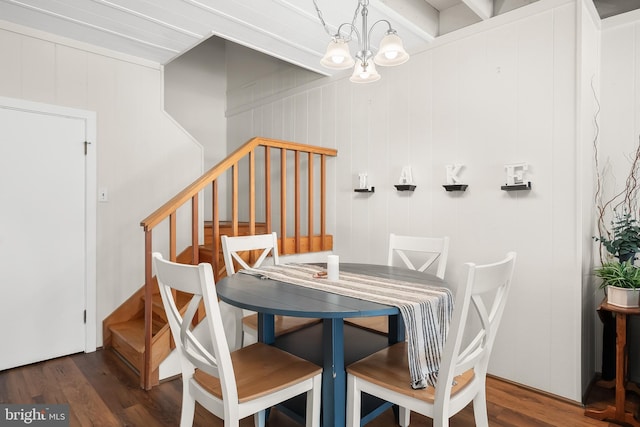 dining room featuring dark wood-type flooring, wood walls, and an inviting chandelier