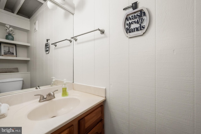 bathroom featuring toilet, wood walls, and vanity