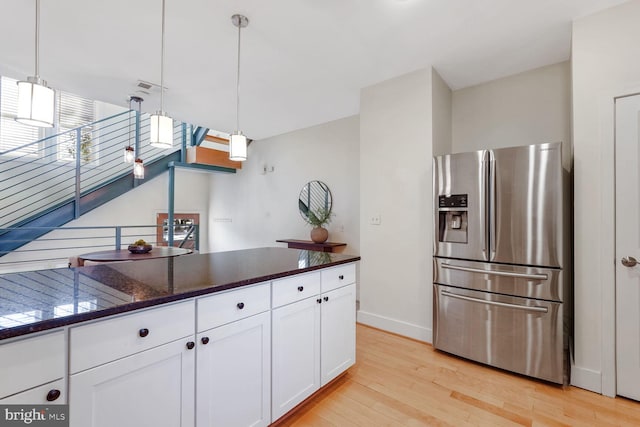 kitchen featuring white cabinets, stainless steel fridge, light hardwood / wood-style floors, and hanging light fixtures