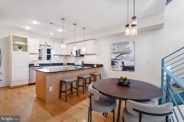 kitchen with light hardwood / wood-style floors, white cabinetry, hanging light fixtures, and appliances with stainless steel finishes