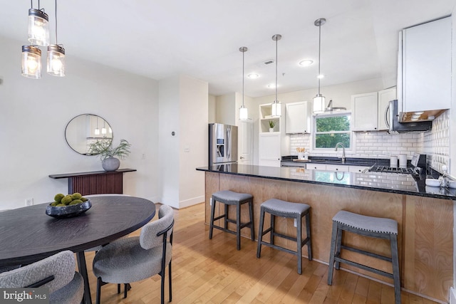 kitchen with white cabinetry, stainless steel appliances, decorative light fixtures, and light wood-type flooring