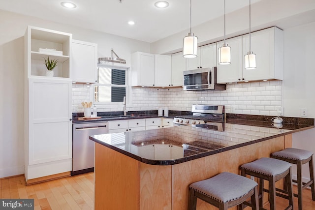 kitchen featuring kitchen peninsula, light hardwood / wood-style floors, a kitchen bar, white cabinets, and appliances with stainless steel finishes