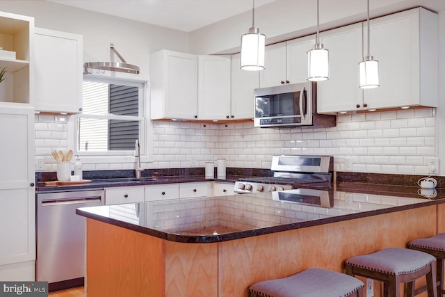 kitchen with sink, decorative light fixtures, a kitchen bar, white cabinets, and appliances with stainless steel finishes