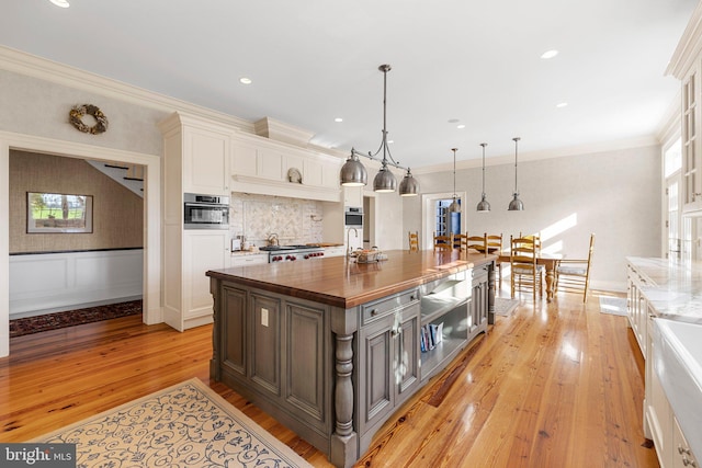 kitchen featuring wood counters, light wood-type flooring, pendant lighting, white cabinets, and a kitchen island