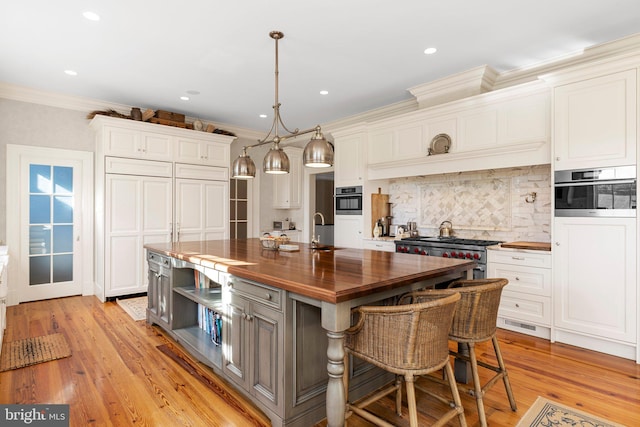 kitchen with appliances with stainless steel finishes, light hardwood / wood-style floors, a kitchen island with sink, and butcher block counters