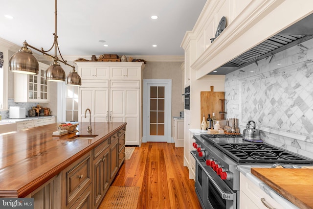 kitchen featuring butcher block counters, hanging light fixtures, stainless steel appliances, crown molding, and custom exhaust hood