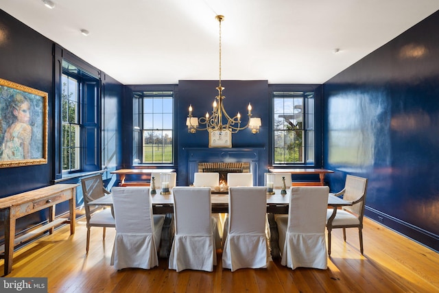 dining space with wood-type flooring, a brick fireplace, plenty of natural light, and a notable chandelier