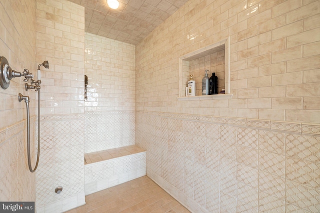 bathroom featuring tile patterned flooring, a tile shower, and tile walls