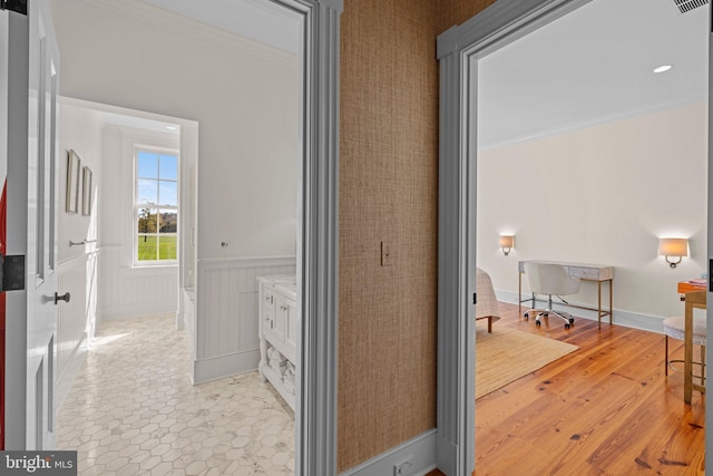 corridor with light hardwood / wood-style floors and ornamental molding