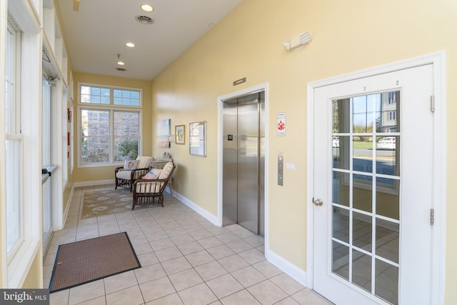 hall with elevator, a healthy amount of sunlight, and light tile patterned flooring