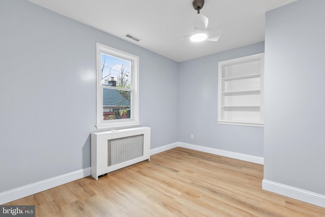 unfurnished room featuring radiator, built in shelves, and light hardwood / wood-style flooring