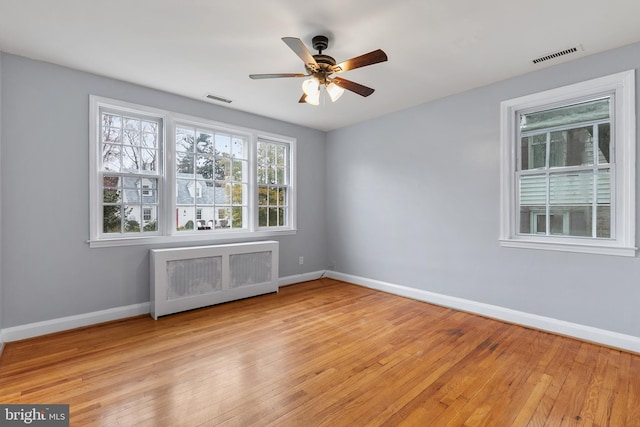 unfurnished room featuring radiator heating unit, light hardwood / wood-style floors, and ceiling fan