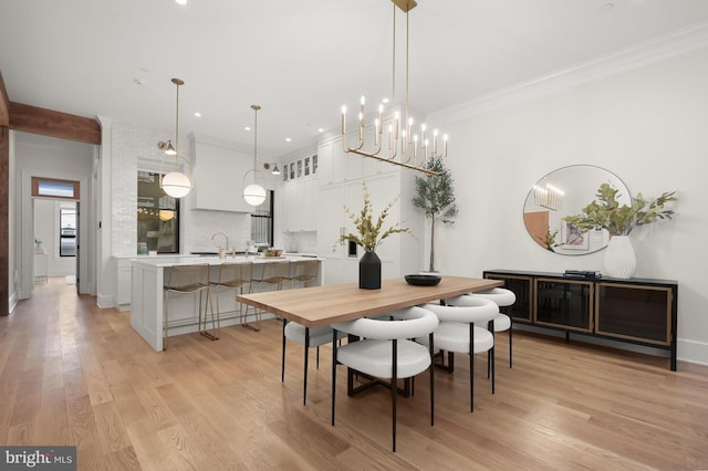 dining room with sink, light hardwood / wood-style flooring, ornamental molding, and a chandelier