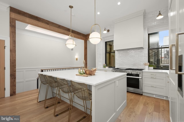 kitchen with high end stainless steel range oven, hanging light fixtures, wall chimney range hood, a kitchen island, and white cabinets