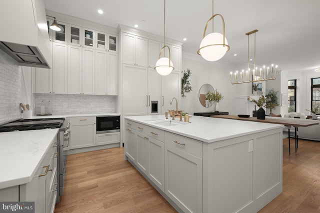 kitchen with pendant lighting, a center island with sink, stainless steel range with gas cooktop, black microwave, and white cabinets