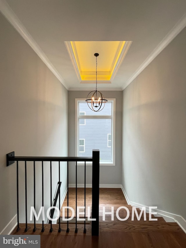 stairway featuring ornamental molding, an inviting chandelier, hardwood / wood-style floors, and a raised ceiling