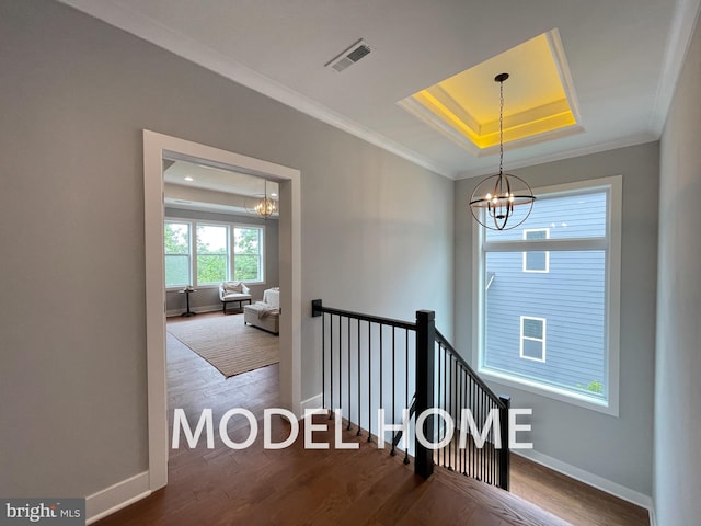 staircase with wood-type flooring, ornamental molding, a raised ceiling, and a notable chandelier