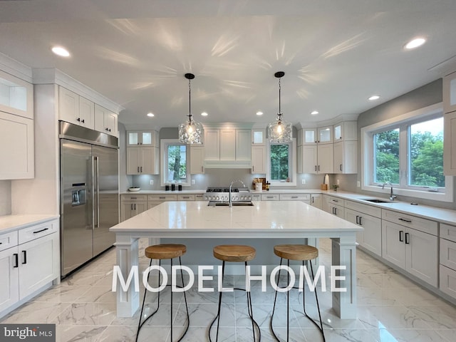 kitchen with built in fridge, sink, pendant lighting, and a center island with sink