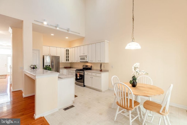 kitchen featuring stainless steel appliances, white cabinetry, a high ceiling, kitchen peninsula, and light hardwood / wood-style flooring