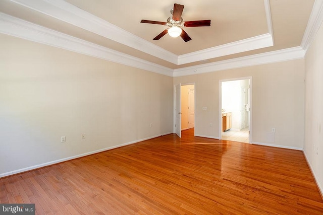 empty room featuring light hardwood / wood-style floors, ceiling fan, a tray ceiling, and ornamental molding