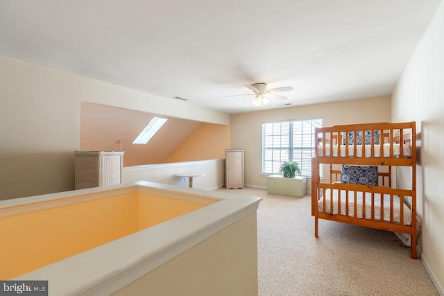 carpeted bedroom with vaulted ceiling with skylight and ceiling fan