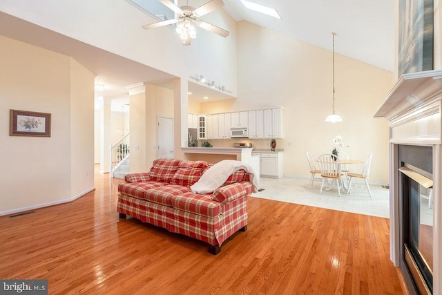 living room with high vaulted ceiling, a skylight, ceiling fan, and light wood-type flooring