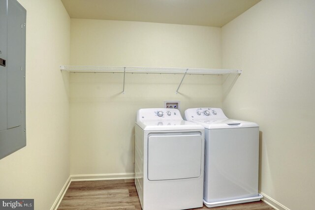 clothes washing area with electric panel, separate washer and dryer, and wood-type flooring