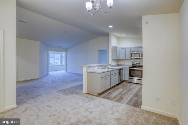 kitchen with kitchen peninsula, stainless steel appliances, lofted ceiling, and light colored carpet