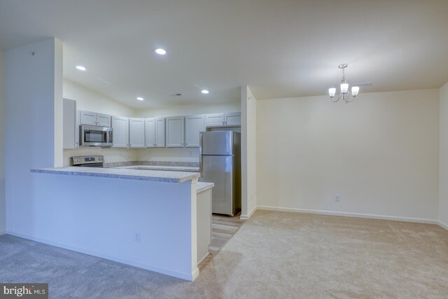 kitchen featuring kitchen peninsula, appliances with stainless steel finishes, an inviting chandelier, light colored carpet, and pendant lighting