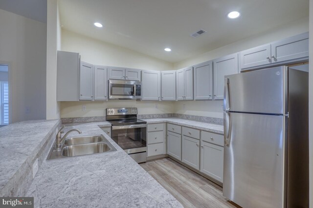 kitchen featuring lofted ceiling, sink, light stone countertops, light wood-type flooring, and appliances with stainless steel finishes