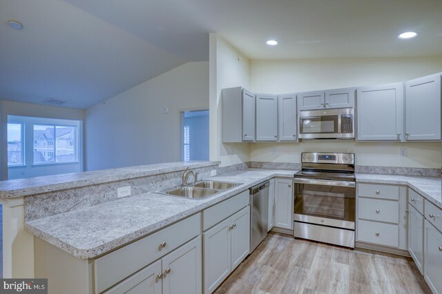 kitchen with stainless steel appliances, sink, vaulted ceiling, light hardwood / wood-style floors, and kitchen peninsula