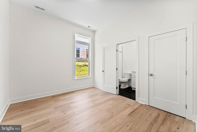 unfurnished bedroom with connected bathroom and light wood-type flooring