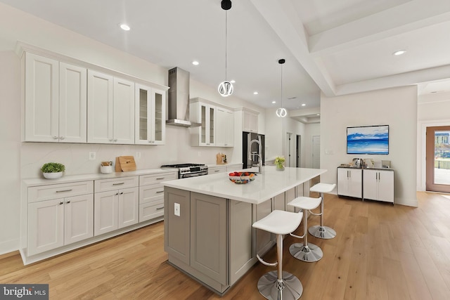 kitchen featuring white cabinetry, a center island with sink, appliances with stainless steel finishes, pendant lighting, and wall chimney range hood