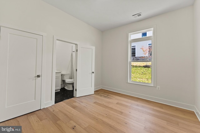 unfurnished bedroom with multiple windows, connected bathroom, and light wood-type flooring