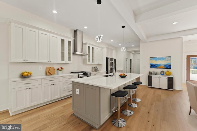 kitchen featuring white cabinetry, a center island with sink, appliances with stainless steel finishes, pendant lighting, and wall chimney range hood