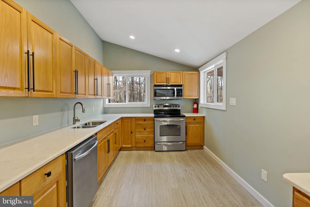 kitchen with appliances with stainless steel finishes, light wood-type flooring, vaulted ceiling, and sink