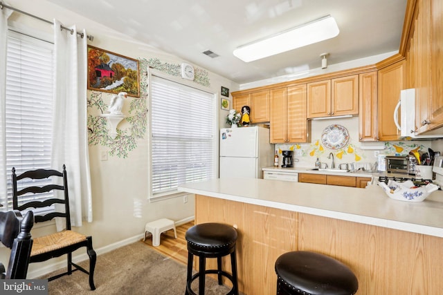 kitchen with a breakfast bar, white appliances, sink, light wood-type flooring, and kitchen peninsula