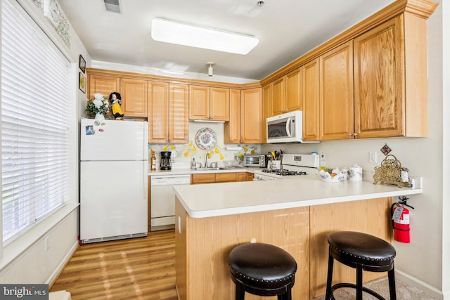 kitchen with kitchen peninsula, white appliances, sink, light hardwood / wood-style floors, and a breakfast bar area