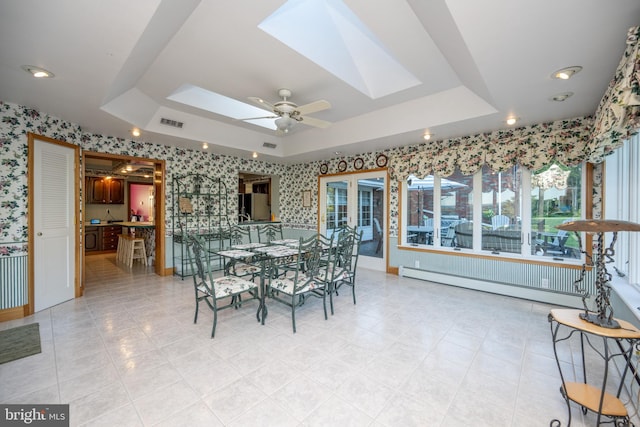 dining room featuring a skylight, a raised ceiling, ceiling fan, and a baseboard heating unit