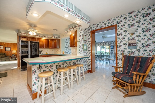 kitchen with black fridge, kitchen peninsula, a kitchen bar, and ceiling fan