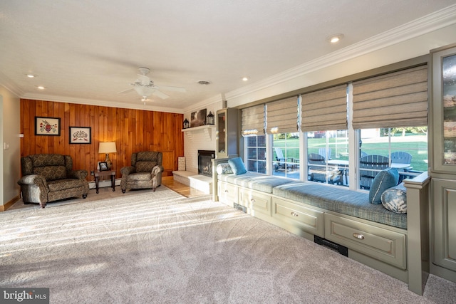 carpeted living room featuring ceiling fan, baseboard heating, crown molding, a brick fireplace, and wooden walls