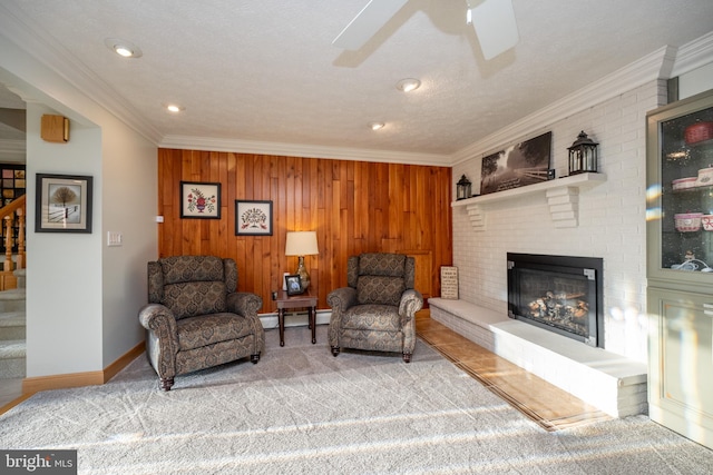 sitting room with wood walls, ceiling fan, baseboard heating, crown molding, and a brick fireplace