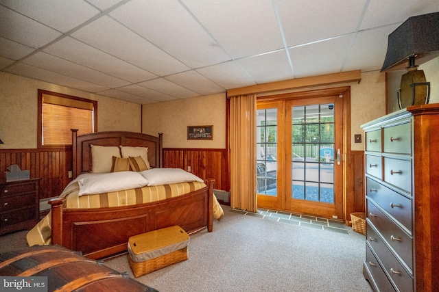 bedroom with access to exterior, carpet, a paneled ceiling, and wood walls