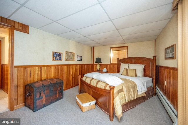 carpeted bedroom featuring a paneled ceiling, wooden walls, and a baseboard heating unit