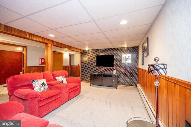 carpeted living room featuring baseboard heating, a paneled ceiling, and wooden walls